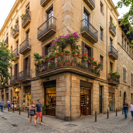 Rue pavée historique de Barcelone. Un bâtiment de coin aux balcons en fer forgé est orné de bougainvilliers et de fleurs.