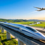 Train TGV argenté sur viaduc et avion décollant au-dessus d'un paysage verdoyant, sous un ciel bleu et soleil couchant.
