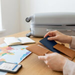 Mains organisant un passeport près d'une carte du monde, un smartphone avec itinéraire, un carnet et une valise ouverte.