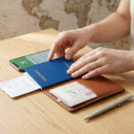 Une personne organise ses documents de voyage : passeport bleu, billets, smartphone avec appli voyage sur une table en bois.