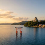 Visiter le lac Biwa : s’évader au cœur de Shiga Vue aérienne du lac Biwa au coucher du soleil. Un torii rouge flotte, le château de Hikone sur une colline, et des maisons traditionnelles bordent le rivage.