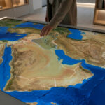 Comprendre la carte du Moyen-Orient : pays et enjeux Main interagissant avec une carte numérique du Moyen-Orient sur une table interactive, montrant frontières et topographie.