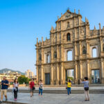 Façade majestueuse en ruine de l'église Saint-Paul à Macao, avec des touristes en bas sous un ciel bleu lumineux.