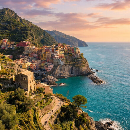 Vue de Manarola, Cinque Terre, avec ses maisons colorées perchées sur une falaise. Mer turquoise et ciel orangé au coucher du soleil.
